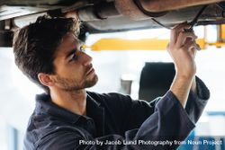 Mechanic repairing car from underneath in auto shop 5olKx4