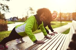 Two women smiling while doing an exercise on a park bench