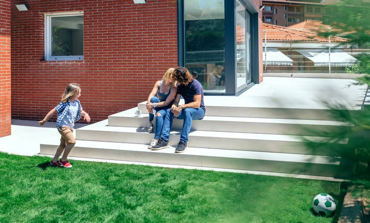 Couple kissing in front new house with son playing