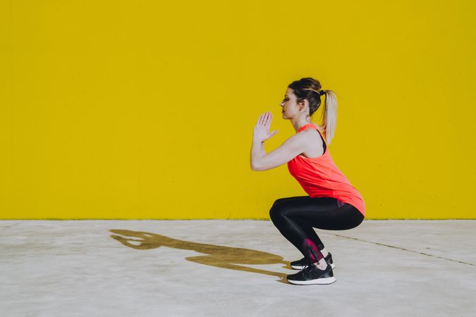 Woman doing squads exercises near a yellow wall