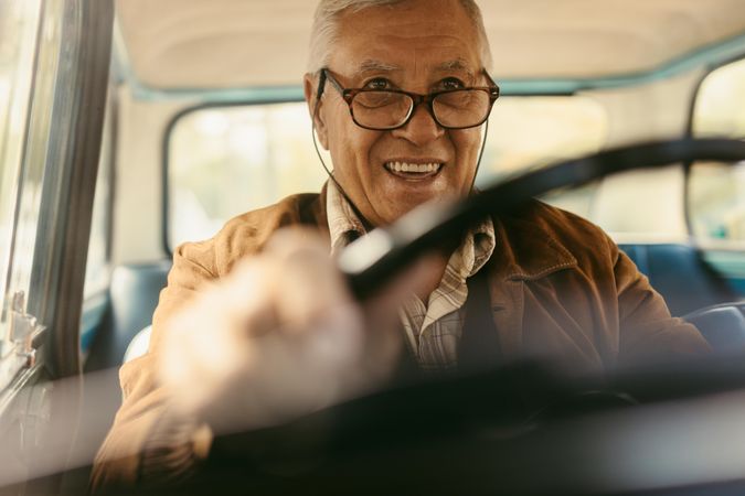 Happy mature man wearing eyeglasses driving a car, shot from inside the car