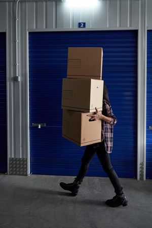 Faceless person carrying heap of boxes