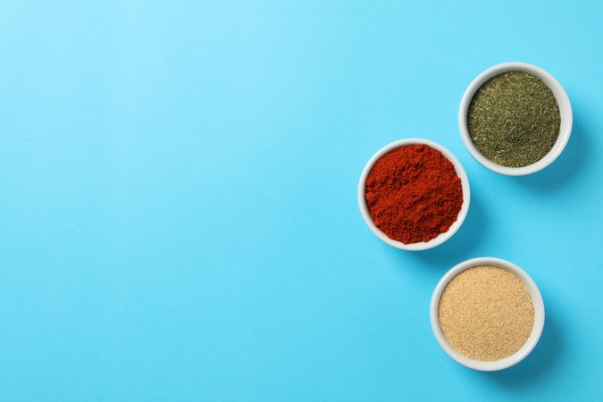Three bowls of spice on blue table, copy space