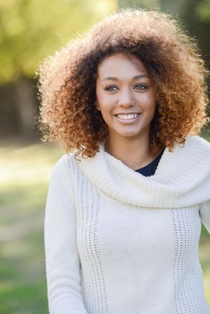 Smiling female in sweater standing outside in park with selective focus