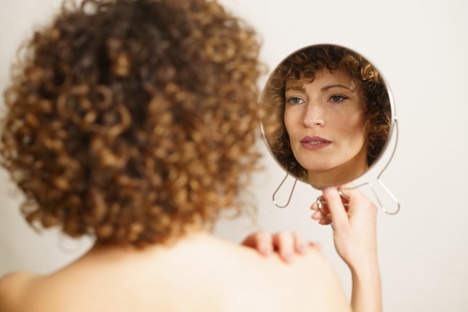 Back of female and her reflection in hand mirror