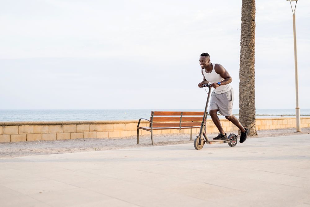Cool adult Black man riding scooter in street