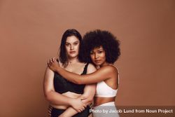 Black model hugging white woman against brown background 48qN7b