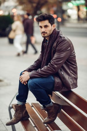 Man in leather coat looking to his side sitting on top of bench