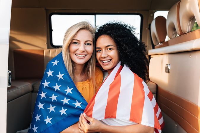 Two women wrapped in American flag in back of a vehicle