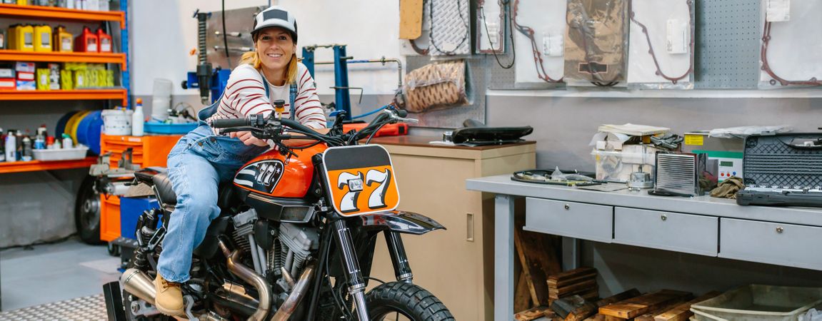Mechanic woman leaning over motorcycle on factory