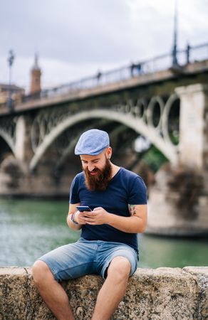 Bearded young man in casual wear using smartphone while walking on quay