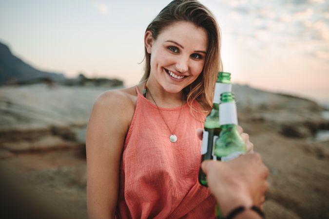 Smiling woman on vacation standing at the beach holding a beer bottle