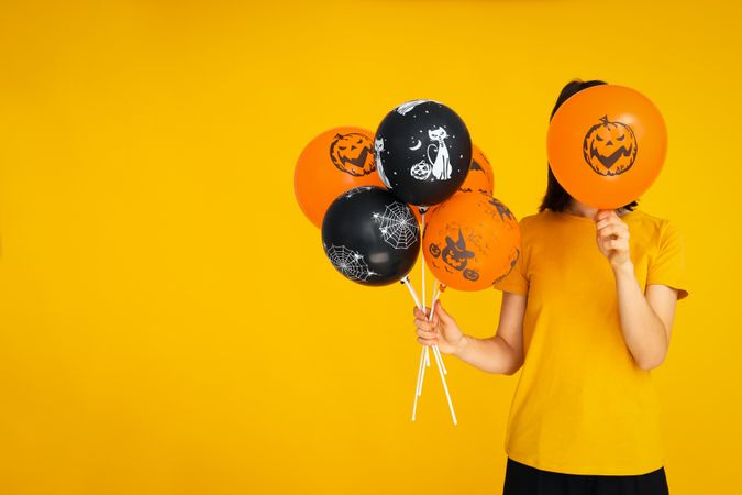 Concept of Halloween, Woman holds Halloween balloons on yellow background