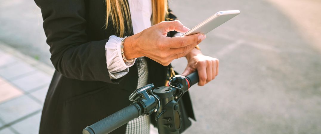 Unrecognizable businesswoman with e-scooter looking at cellphone
