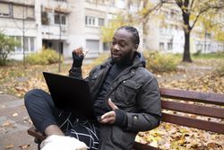 Young Black Man on Video Call Outdoors with Laptop in Park.