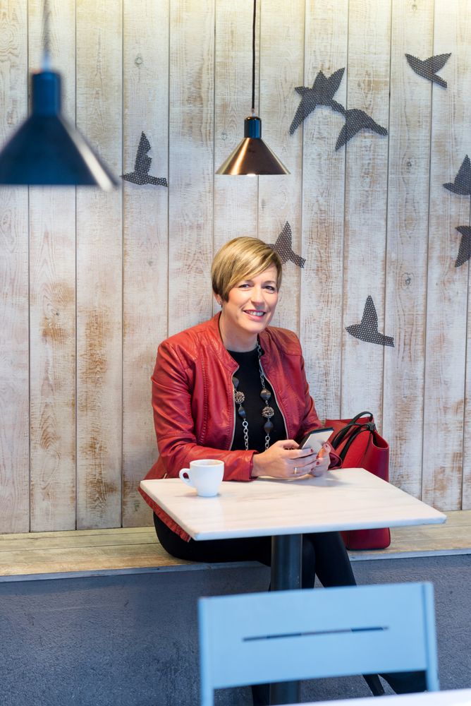 Smiling woman in red coat sitting in cafe texting on phone