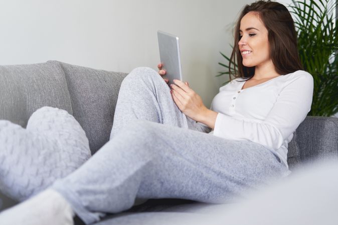 Smiling woman browsing on tablet and sitting on settee