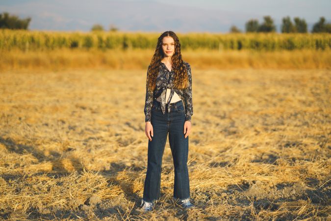 A Young Woman is Standing in a Beautiful Field of Dry Grass Surrounded by a Scenic Background