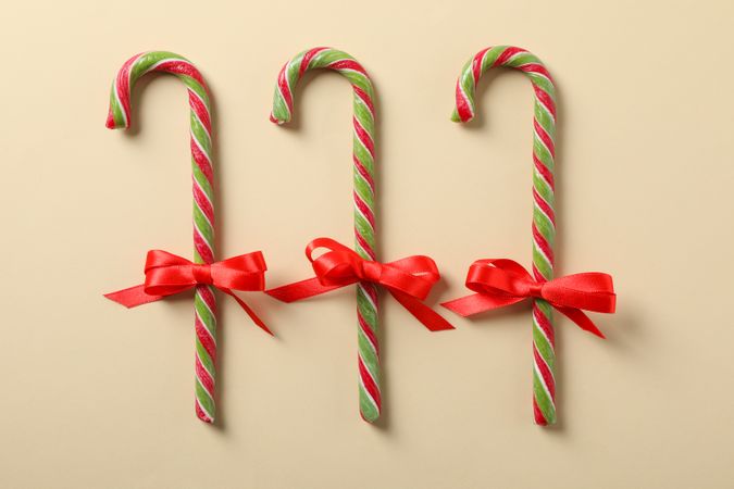 Sweet candy canes with bow on color background. Flat lay