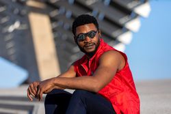 Black man wearing round sunglasses and red vest sitting outside