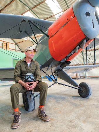 Pilot waiting beside retro plane in hangar