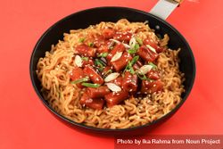 Pan of noodles topped with Korean rice cakes with red background bGakl5