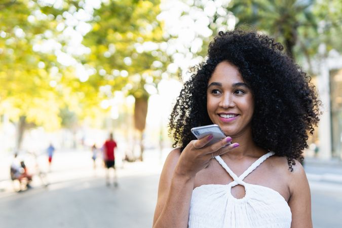 Smiling Black woman recording audio message on smartphone