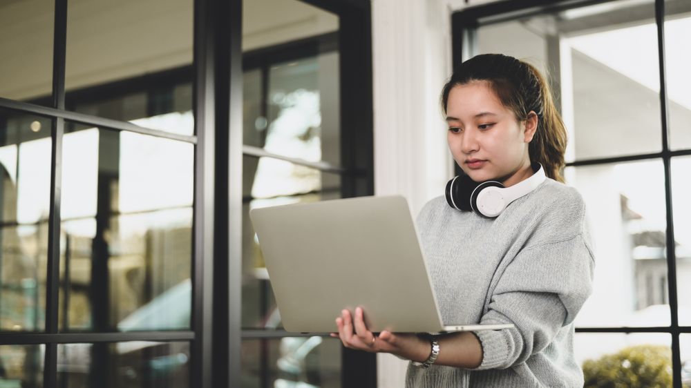 Young Asian woman with headphones holding laptop video chatting with friends.