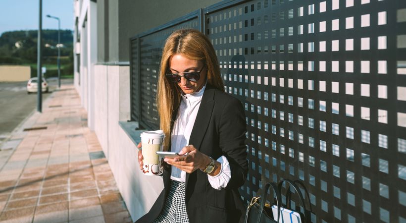 Businesswoman using mobile and drinking coffee
