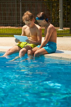 Boys on poolside browsing tablet