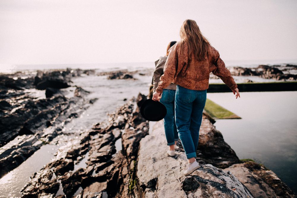 Two young women walking along the rocks on the beach