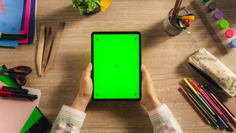 Top Down View of an Anonymous Creative Young Man Holding Tablet Computer with Mock Up Green Screen Chromakey Display Vertically. Designer or an Art Student Viewing an Online Presentation