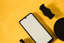 Mock up phone on yellow table with accessories, shadow and copy space