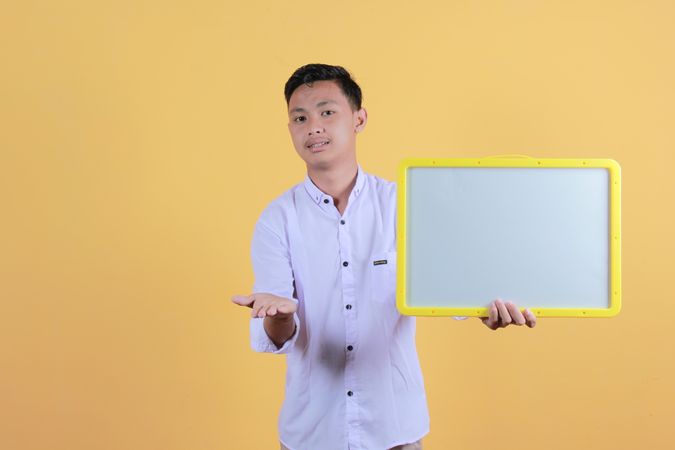 Portrait of a young man in yellow backdrop holding a blank note board