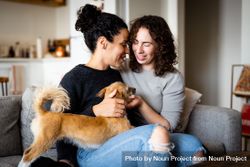 Female couple sitting close by and relaxing at home on sofa with dog bGee25