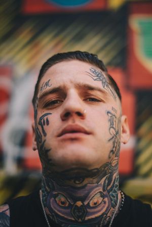 Man with face and neck tattoos and nose ring against colorful blurred background