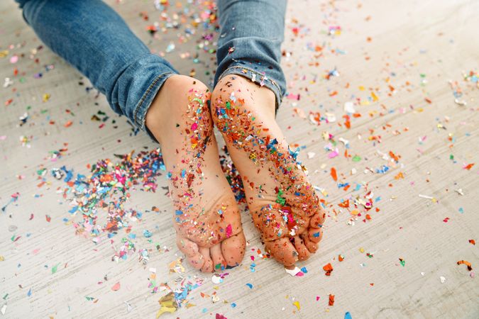 Crop boy on wooden floor with feet covered with confetti