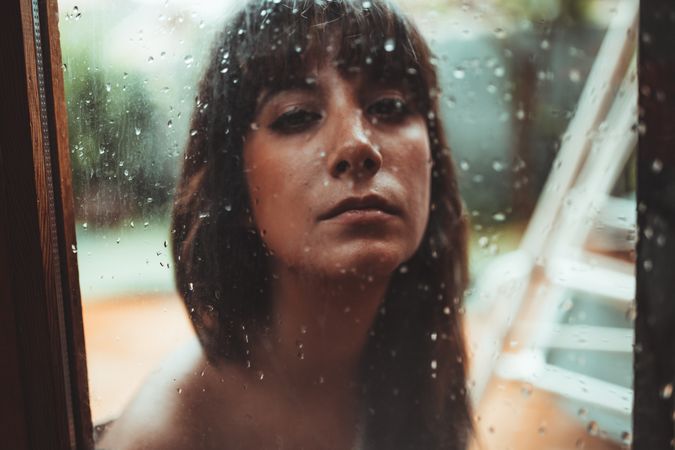 Woman looking at camera behind a wet glass