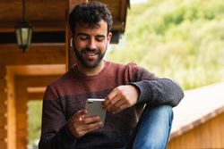 Smiling man listening to music in earbuds on terrace