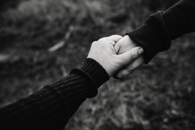 Grayscale photo of two people holding hands