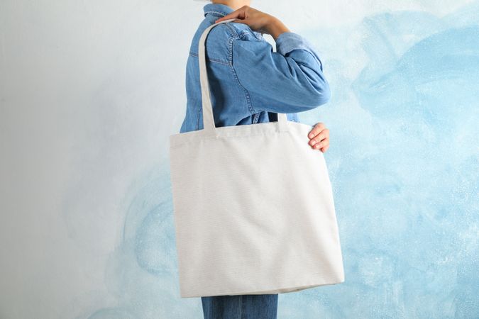 Young woman holding tote bag against blue background, empty space
