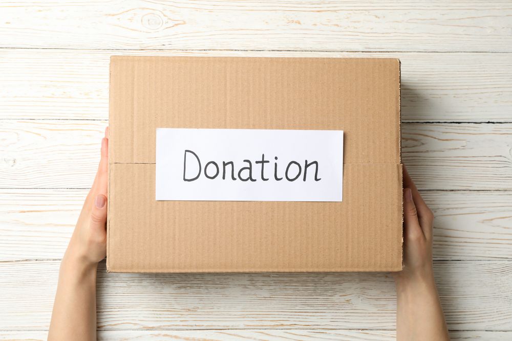 Female hands hold paper box with text Donation on wooden background