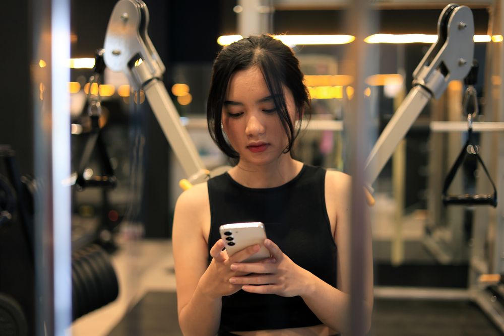 Young Female Sitting on Bench at the Gym with Mobile Phone