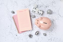 Piggy bank, gift box, Christmas decor and shopping list on marble background, top view