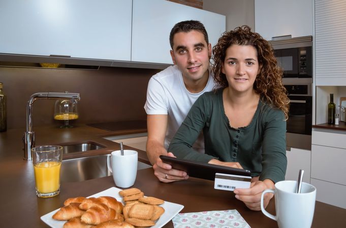 Smiling couple with credit card and tablet at breakfast