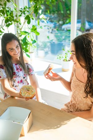 Joyful female friends eating donuts at cafe