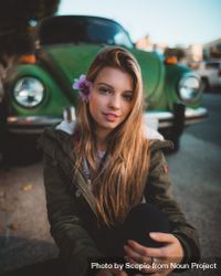 Woman in green jacket smiling and sitting on ground near green Volkswagen car 5zpVgb