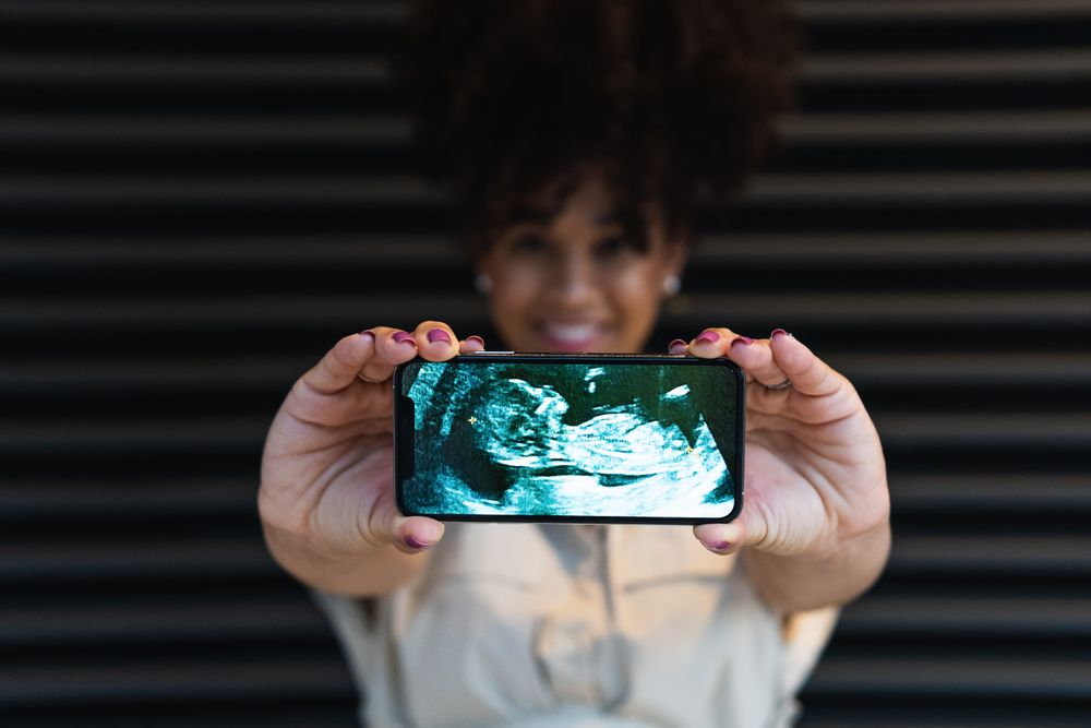 Smiling Black woman showing smartphone screen with baby ultrasound
