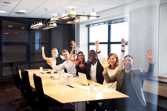 Colleagues sitting in a row with their arms up in celebration in meeting room