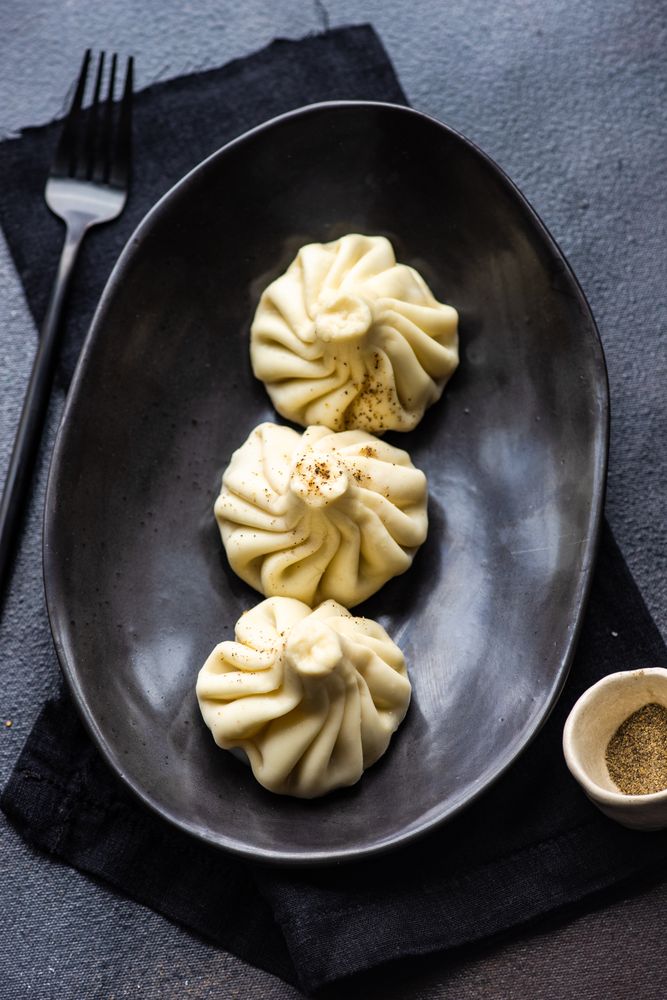 Top view of plate of three Georgian khinkali dumplings on dark plate with napkin